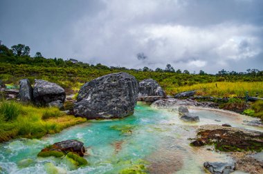 Purac, Cauca 'daki San Juan kaplıcalarının sakin manzarasında yemyeşil ve kayalık arazilerle çevrili canlı turkuaz su sergileniyor.