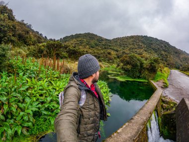 Bir adam Purace, Cauca 'daki San Juan kaplıcalarının manzarasının tadını çıkarıyor. Etrafı yemyeşil ve dağlık arazilerle çevrili..