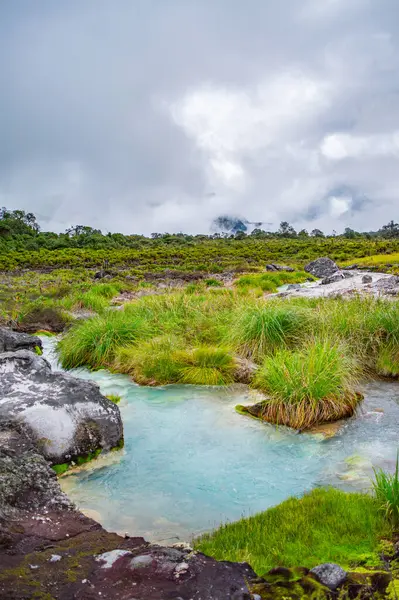 Purac, Cauca 'daki San Juan kaplıcalarının sakin manzarası, yemyeşil ve bulutlu bir gökyüzünün altındaki kayalık araziyle çevrili.