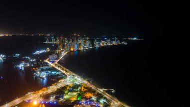 Cartagena 'nın gökdeleninin göz kamaştırıcı hava manzarası gece aydınlandı, kıyı boyunca modern binalar ve canlı şehir ışıkları suya yansıdı.