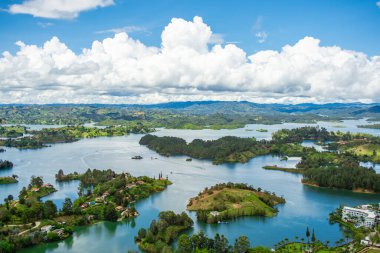 Guatape 'in göz kamaştırıcı hava manzarası, canlı göl manzarasını ve mavi gökyüzünün altında kabarık bulutlu yemyeşil tepeleri gösteriyor.