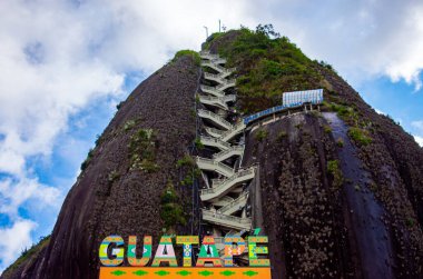 Guatape, Antioquia 'daki Peol Taşı' nın göz kamaştırıcı manzarası, dolambaçlı merdiveni ve mavi gökyüzünün altında canlı bir çevresi var.