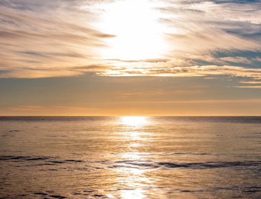 Güzel bir günbatımı, sakin okyanus sularına altın bir parıltı saçar. Gökyüzünü pastel renklerle aydınlatır. Tatil için mükemmel bir ilham kaynağı.