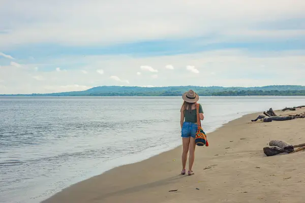 Rincon del Mar, Sucre, Kolombiya yakınlarındaki kumlu bir plajda gezinen bir kadın, sakin okyanus ve yemyeşil tepelerin çarpıcı manzarasıyla
