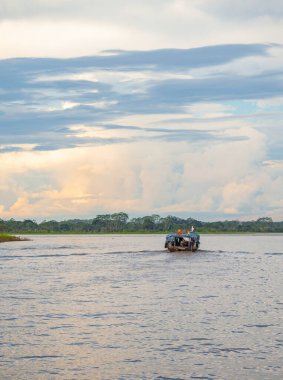 Kolombiya 'nın Leticia kentindeki sakin sularda gezinen, yemyeşil tropikal yağmur ormanlarıyla çevrili bir teknenin manzarası..