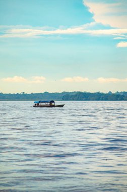 Amazon Nehri 'nde süzülen bir teknenin huzurlu manzarası. Leticia, Amazonas, Kolombiya' da mavi gökyüzünün altında yemyeşil bir yeşil ile çevrili..