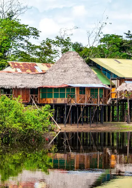 Çiçekli yeşilliklerle çevrili ve Leticia, Amazonas, Kolombiya 'nın sakin sularına yansıyan ayaklıklar üzerinde geleneksel bir Amazon kulübesinin pitoresk bir görüntüsü..