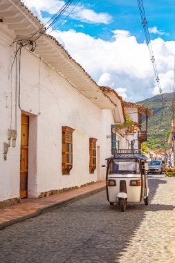Kolombiya, Santa F de Antioquia 'daki kaldırım taşı caddesi boyunca geleneksel bir tuk-tuk ile büyüleyici bir koloni mimarisi..