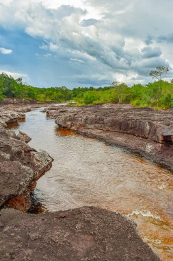 Guaviare, Kolombiya 'da bulutlu bir gökyüzünün altında kayalık arazide süzülen huzurlu bir nehrin manzarası.