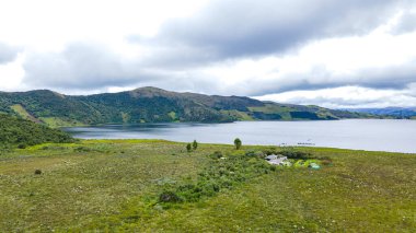 Nario, Kolombiya 'daki Laguna del Cumbal' ın sakin manzarası yemyeşil tarlalar, uzak tepeler ve bulutlu bir gökyüzünün altında sakin bir göl.