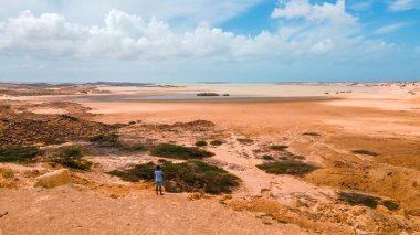 La Guajira, Kolombiya 'daki yayılan çöl manzarasının panoramik görüntüsü, canlı toprak tonlarını ve kayalık arazide yalnız bir figürü gözler önüne seriyor..