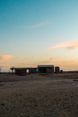 La Guajira, Kolombiya 'da renkli bir alacakaranlık gökyüzünün altında basit yapılar barındıran sakin bir manzara..