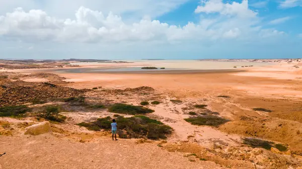 La Guajira, Kolombiya 'daki yayılan çöl manzarasının panoramik görüntüsü, canlı toprak tonlarını ve kayalık arazide yalnız bir figürü gözler önüne seriyor..