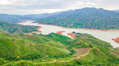 Kolombiya, Cauca 'daki Salvajina Barajı' nın nefes kesici manzarası bulutlu bir gökyüzünün altında yemyeşil tepeler ve sakin sular sergiliyor..