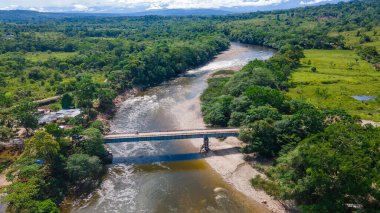Şaşırtıcı hava manzarası nehri geçen bir köprüyü gösteriyor, Putumayo, Kolombiya 'da yemyeşil manzaralarla çevrili..