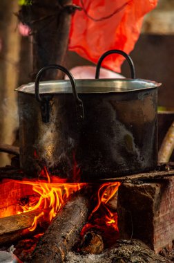 Siyah bir tencere, Putumayo, Kolombiya 'daki geleneksel yemek pişirme yöntemlerini tasvir eden odun ve dumanla çevrili canlı bir ateşin üzerinde oturur..