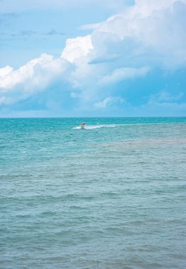 Turkuaz denizin sakin bir görüntüsü ve Rosario Adası, Cartagena, Kolombiya yakınlarında parçalı bulutlu bir gökyüzünün altında yelken açan bir tekne..