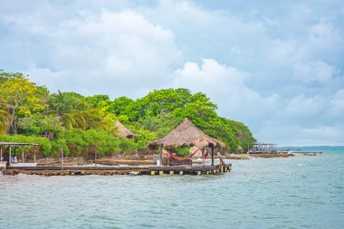 Rosario Adaları 'ndaki tropik bir adanın güzel manzarası. Palmiye ağaçları, hamak ve su kenarındaki ahşap yapılar..