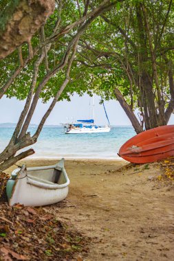 Rosario Adaları 'nda sakin bir sahil manzarası beyaz bir tekne, yemyeşil bir tekne ve uzaktaki bir yelkenli..