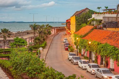 Renkli binalar Cartagena 'nın tarihi merkezindeki liman caddesi boyunca uzanır, yemyeşil ve sakin bir okyanus manzarası vardır..