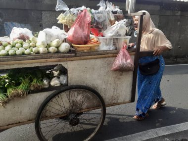 Jakarta, Endonezya, Aralık 01.2022: Bir anne sebze arabasını sokağa itiyor, köylerdeki gezgin sebze satıcıları ona sebze sunuyor..