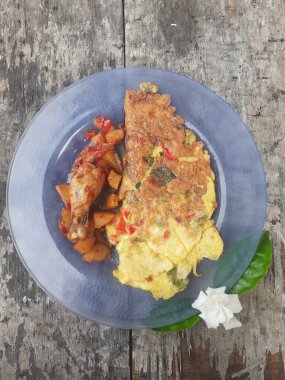 Kahvaltı spesiyali, doldurulmuş omlet menüsü, patates ve kızarmış tavuk tabakta. Ev yapımı. Ahşap arka plan..
