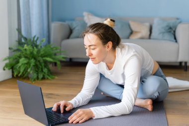 Spor giyimli genç bir kadın, evde pratik yapmak için dizüstü bilgisayarında yoga dersi arıyor. Boşluğu kopyala.