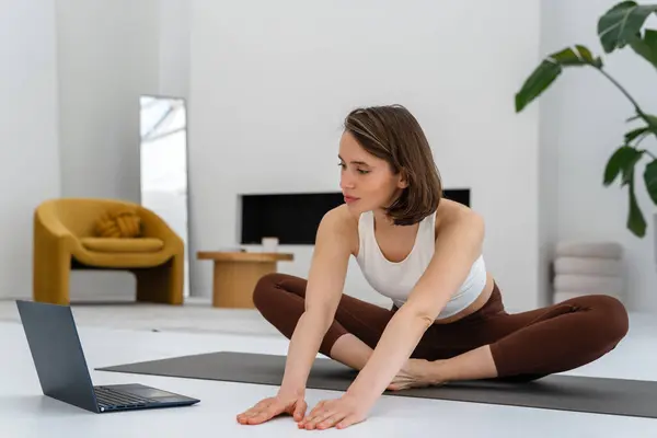 Kadın laptopunda online bir ders kullanarak yoga yapıyor. Spor eğitimi. Sağlıklı yaşam tarzı kavramı, kadın sağlığı..