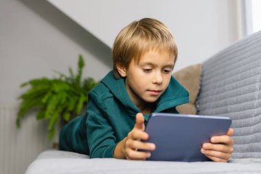 Çocuk oturma odasındaki kanepede bir tabletin üzerinde bir ekranın arkasında zaman geçiriyor. Dijital cihaz. Teknolojiler.