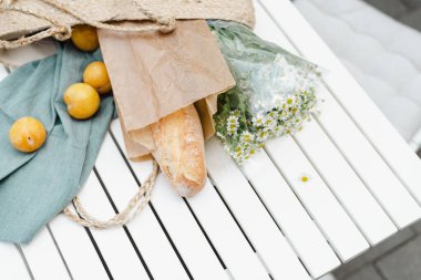 Bir buket papatya çayı, olgun sarı erikler ve saman poşetinde taze bir baget..