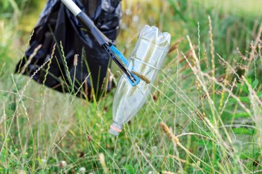 Çöpe atılmış plastik bir şişeyi çimenden siyah bir çöp torbasına koyan bir gönüllü..
