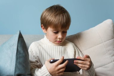 Çocuk oturma odasındaki kanepede bir tabletin üzerinde bir ekranın arkasında zaman geçiriyor. Dijital cihaz. Teknolojiler.