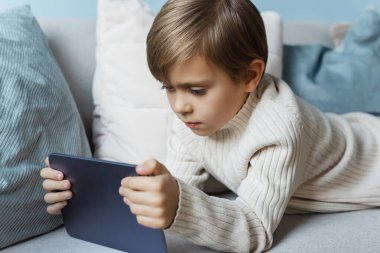 Oğlan evdeki kanepede dinleniyor ve tablet kullanıyor..