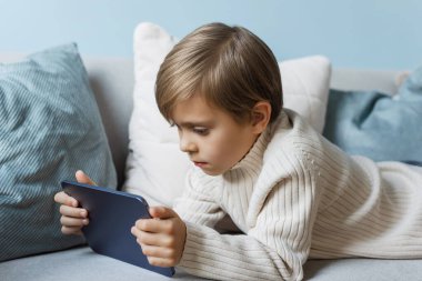 Çocuk evdeki kanepede dinleniyor ve dijital tablet kullanıyor..