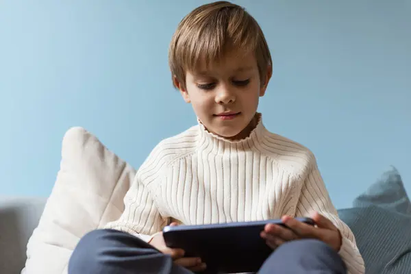 Çocuk oturma odasındaki kanepede bir tabletin üzerinde bir ekranın arkasında zaman geçiriyor. Dijital cihaz. Teknolojiler.