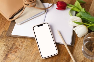 Masasında kalem, not defteri ve moda çantası olan beyaz ekranlı cep telefonunun üst görüntüsü..