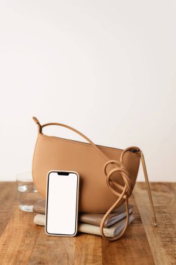 Kalem, not defteri ve ahşap bir masanın üzerindeki moda çantasıyla beyaz ekranlı cep telefonu görüntüsü.