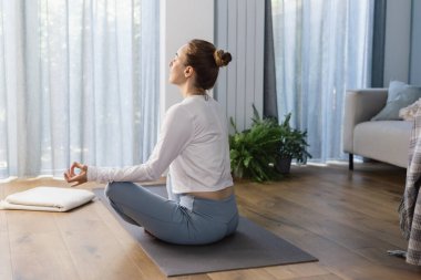 Genç bir kadın evde meditasyon yapıyor. Akıl sağlığı kavramı ve kadın sağlığı, farkındalık..