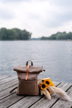 Traveler's backpack and a bunch of sunflowers lie on a pier. clipart