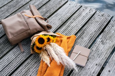 Gezginin sırt çantası, günlük ve bir demet ayçiçeği rıhtımda yatıyor..