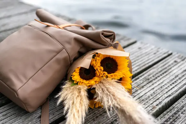 stock image Traveler's backpack and a bunch of sunflowers lie on a pier.