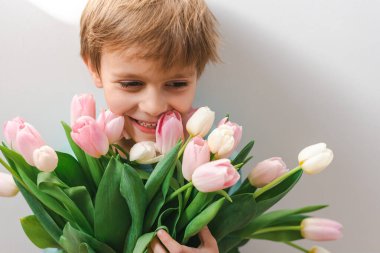 Küçük bir çocuk pembe ve beyaz lalelerden bir buket tutuyor..