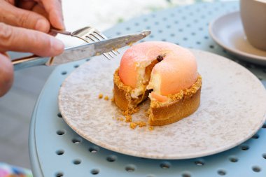 Tanımlanamayan kadın elleri bir çatal ve bıçakla şeftalili kek tabağını kapatıyor..