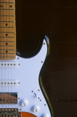 Büyüleyici bir tasarımı olan bir elektro gitar koyu kahverengi bir ahşap arka planın önünde oturur.