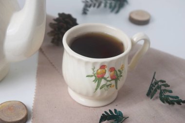 Bir fincan çay ve seramik malzemeli, kuş desenli, beyaz arkaplanlı beyaz bir çaydanlığın fotoğrafını çek.