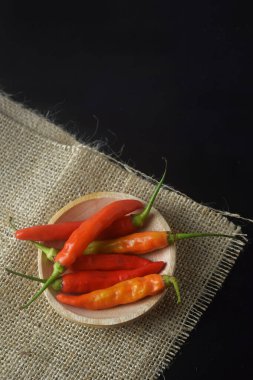 Kırmızı biberler ahşap bir tabakta ve siyah seramik bir hasırda.