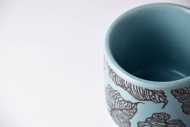 Açık mavi bir fincanın, beyaz izole bir arkaplanda çiçek motifli yakın plan fotoğrafı.