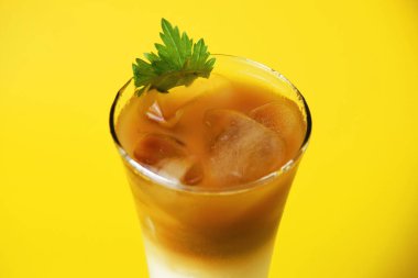 Karpuz şurubu katmanlı bir pandan buzlu kahve içeceği, sarı arka planda uzun bir bardakta sütlü ve çikolatalı kahve.