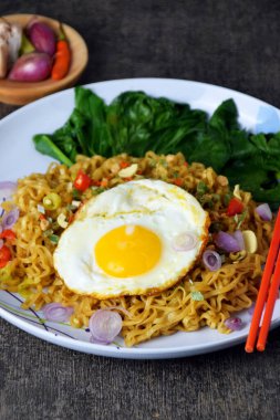 Closeup photo of fried noodles with sunny side up egg and mixed vegetables on a plate with a cement background clipart