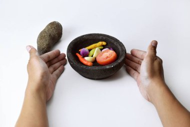 Bir adam, kırmızı biber, soğan ve domatesleri taştan yapılmış bir havan topunda kullanarak acı biber sosu yapmak için gerekli malzemeleri gösteriyor. Beyaz arkaplanı ayır